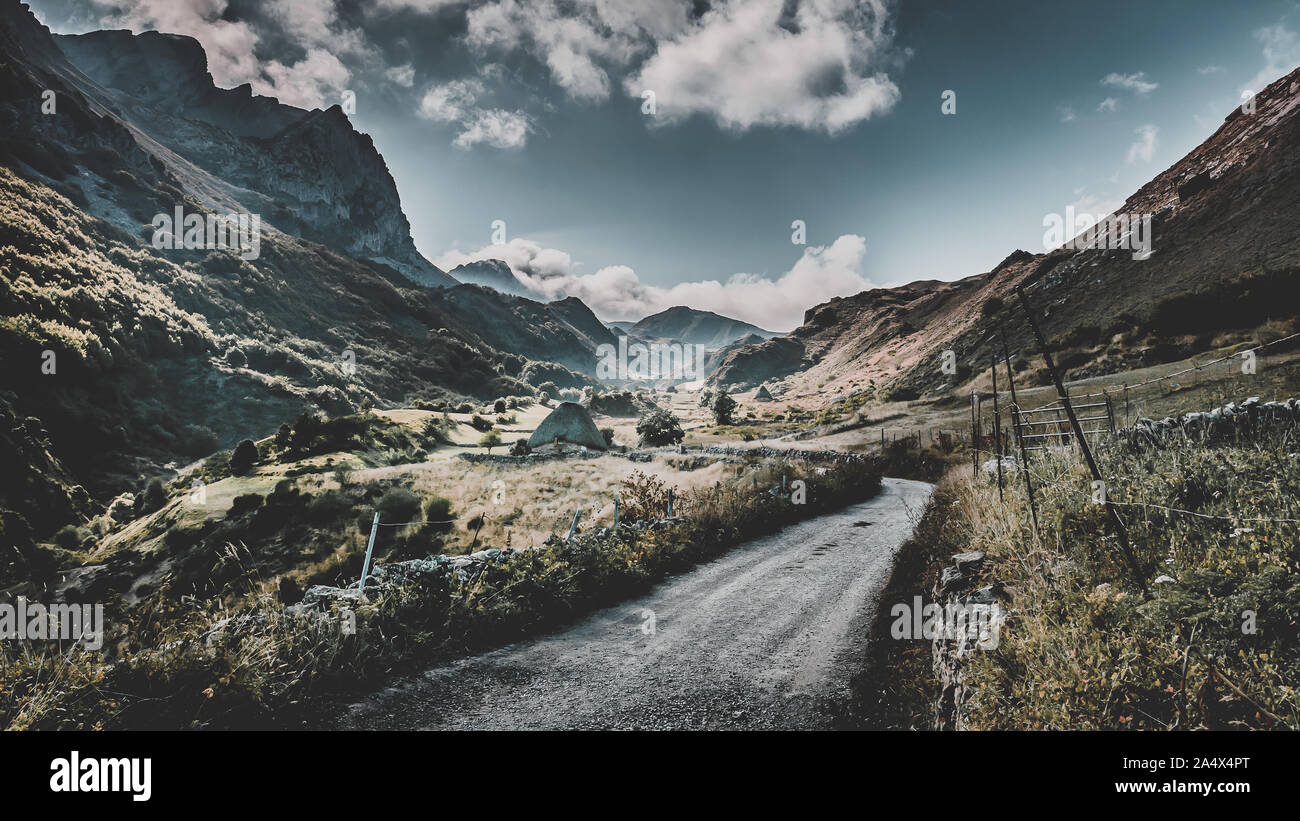 Teitos im Naturpark von Somiedo, La Peral, Asturien, Spanien. alte Häuser der Hirten zwischen Gebirge mit Straße durch das Tal. Stockfoto Teitos im Naturpark von Somiedo, La Peral, Asturien, Spanien. alte Häuser der Hirten zwischen Gebirge mit Straße durch das Tal. Stockfoto
