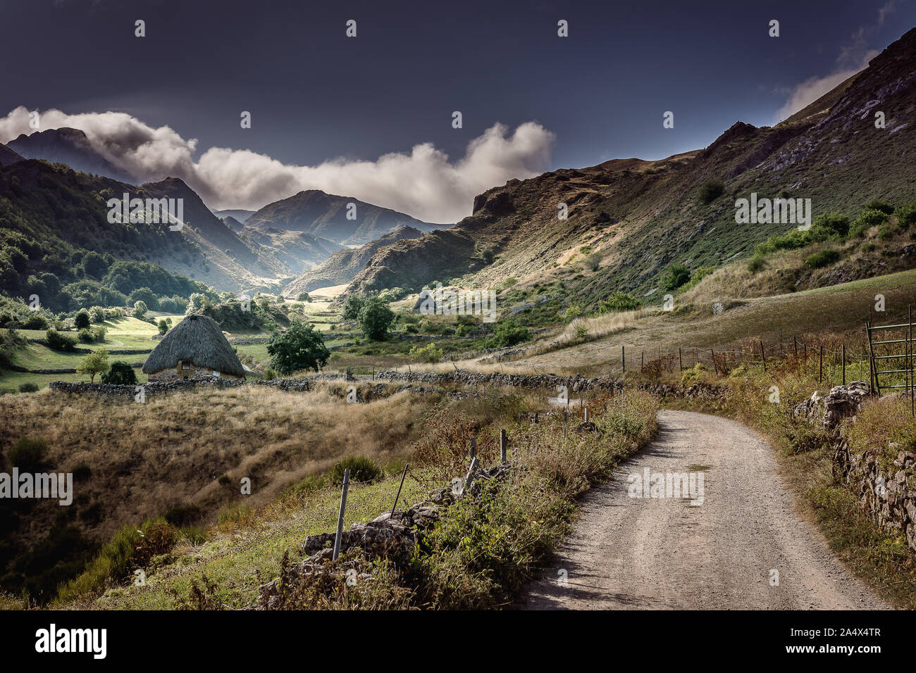 Teitos im Naturpark von Somiedo, La Peral, Asturien, Spanien. alte Häuser der Hirten zwischen Gebirge mit Straße durch das Tal. Stockfoto Teitos im Naturpark von Somiedo, La Peral, Asturien, Spanien. alte Häuser der Hirten zwischen Gebirge mit Straße durch das Tal. Stockfoto