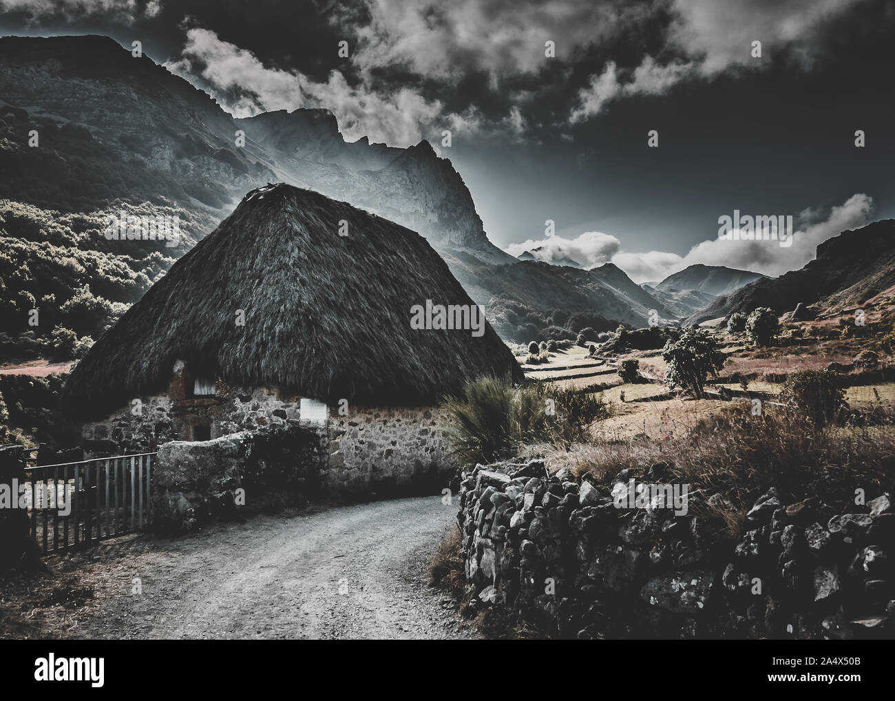 Teitos im Naturpark von Somiedo, La Peral, Asturien, Spanien. alte Häuser der Hirten zwischen Gebirge mit Straße durch das Tal. Stockfoto Teitos im Naturpark von Somiedo, La Peral, Asturien, Spanien. alte Häuser der Hirten zwischen Gebirge mit Straße durch das Tal. Stockfoto