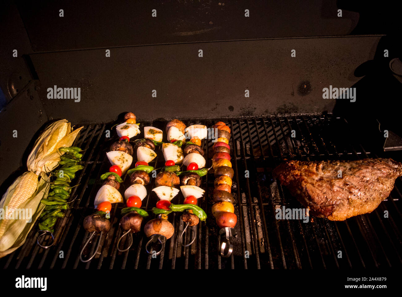 Mais und Fleischspieße und einem riesigen Tri tip steak Koch auf ein BBQ am Abend. Stockfoto