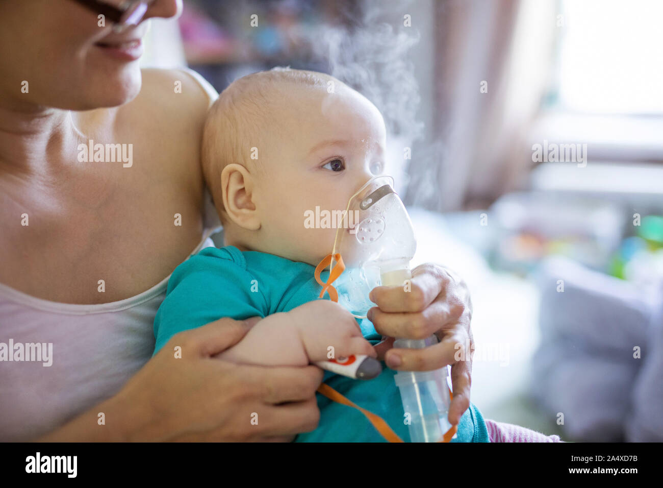Baby Girl, die Inhalation mit Zerstäuber sitzend auf Mama's Schoß zu Hause Stockfoto