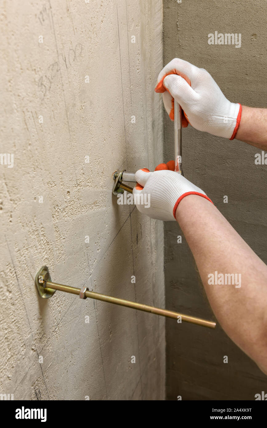 Ein Arbeitnehmer ist zur Festsetzung in einer Wand der Schrauben. Weiter ein Frame mit einem eingebauten Tank befestigen. Stockfoto