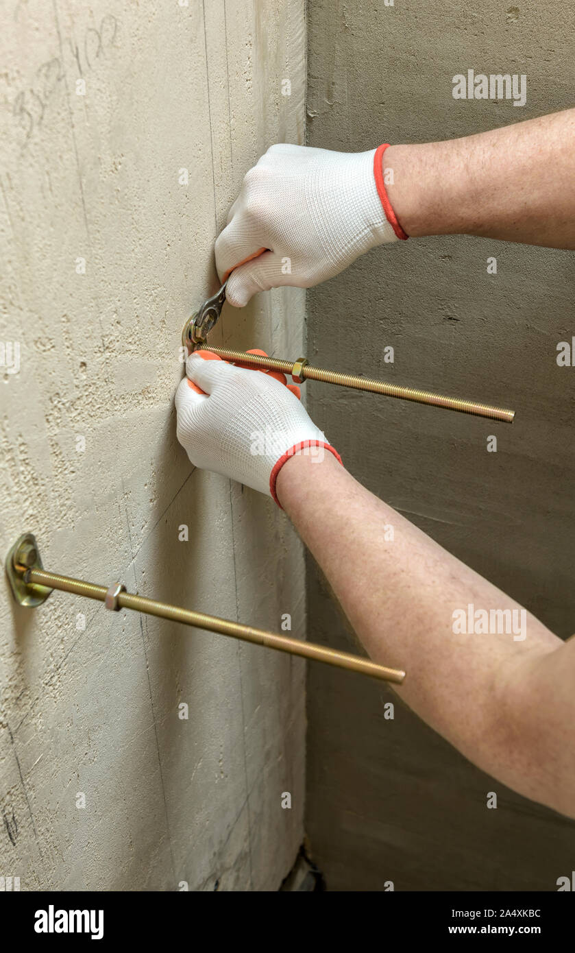 Ein Arbeitnehmer ist zur Festsetzung in einer Wand der Schrauben. Weiter ein Frame mit einem eingebauten Tank befestigen. Stockfoto
