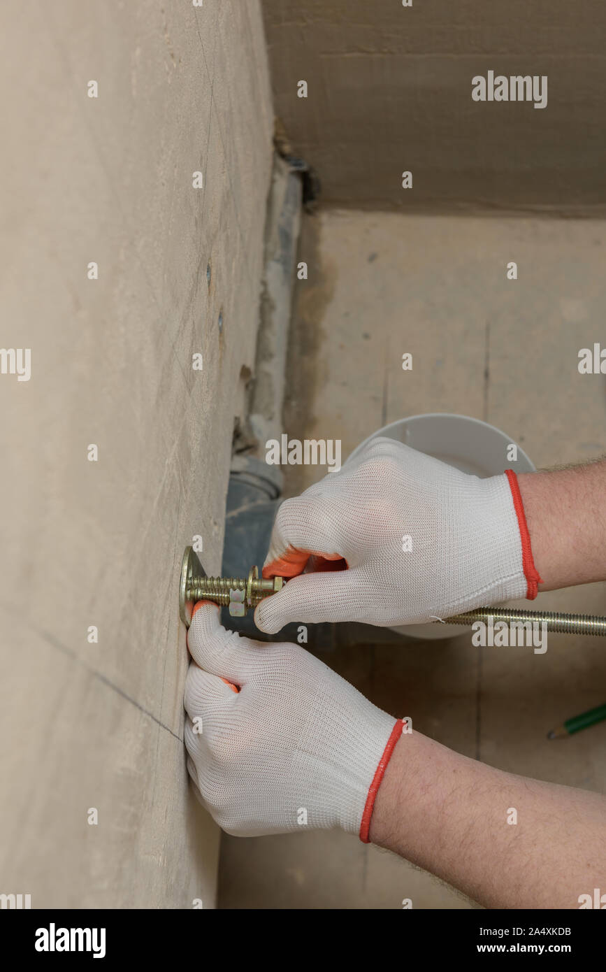 Ein Arbeitnehmer Ein Arbeitnehmer zur Festsetzung in einer Wand der Schrauben. Weiter ein Frame mit einem eingebauten Tank. Eine Wand der Schrauben befestigen. Weiter ein Frame mit einem Bu befestigen Stockfoto