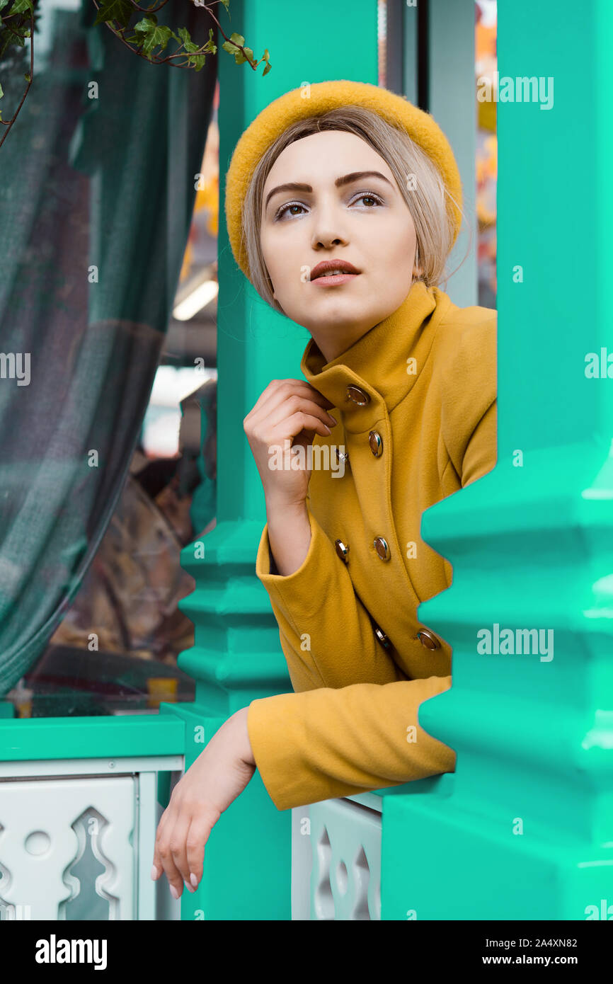 Schöne junge Frau in einem Senffarbenen Mantel und Kappe Stockfoto