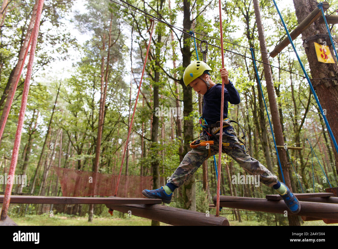 Little Boy in Helm seine Freizeit im Abenteuer Spielplatz verbringen. Das Kind geht auf ein Stahlseil, das Festhalten an den Seilen. Stockfoto