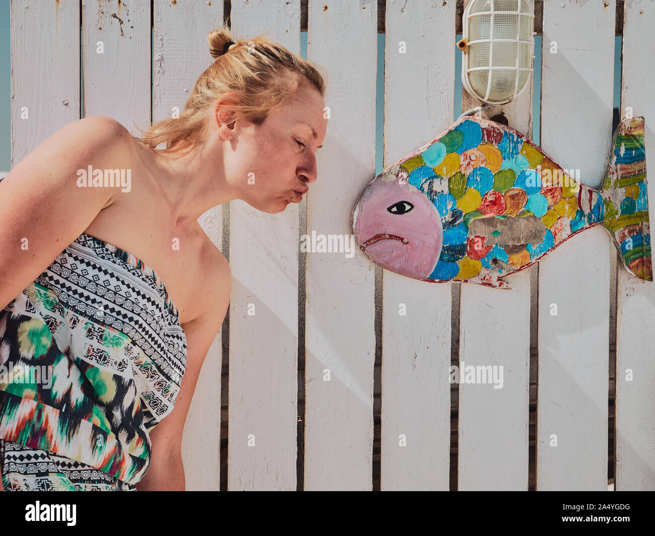 Junge blonde Mädchen küssen wütend bunte Fische auf weißem mediterranen Holz- Hintergrund Stockfoto