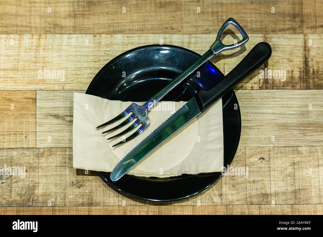 Die Messer und Gabel in eine schwarze Platte mit Seidenpapier auf dem hölzernen Tisch Stockfoto