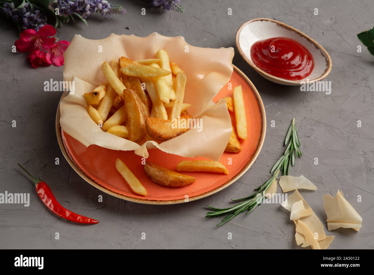 Pommes frites in einem orange Platte und Tomatensauce in eine Tasse auf einem grauen Hintergrund Stockfoto