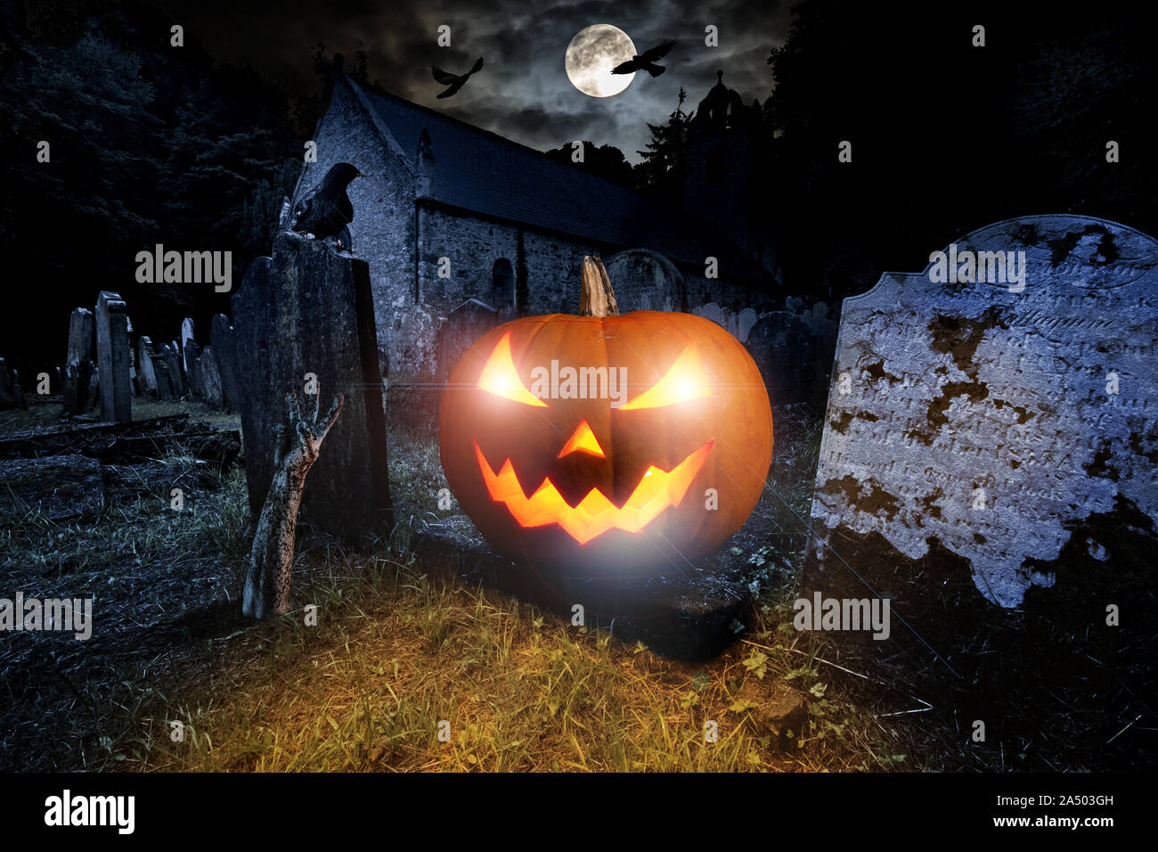 Orange leuchtende Halloween Kürbis mit scyry zombie Hand auf dem alten Friedhof vor Vollmond Black Raven Kirche dunkle Nacht gruselige Horror Hintergrund Stockfoto