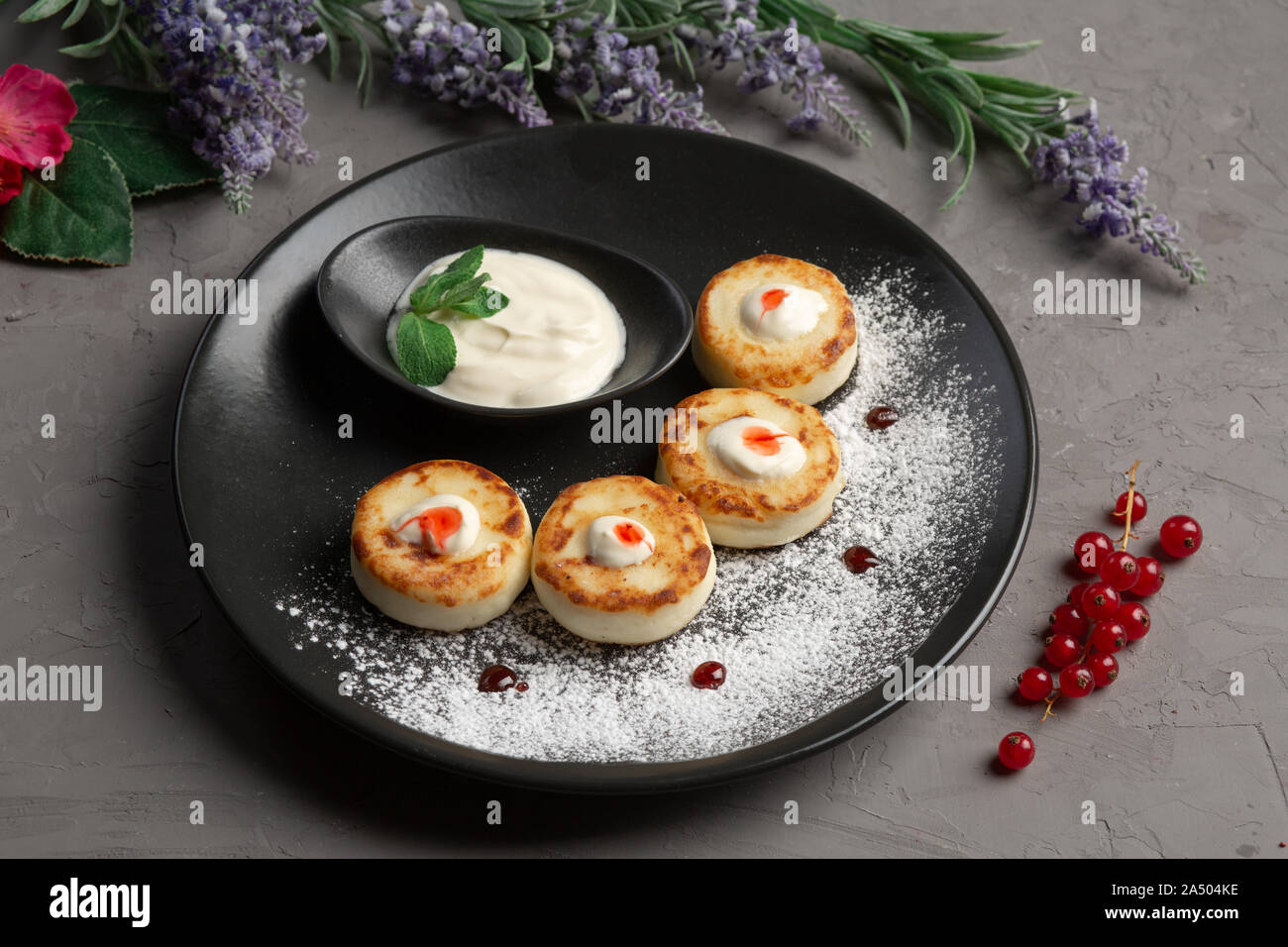 Pfannkuchen mit Sauerrahm in eine schwarze Platte mit Puderzucker auf grauem Hintergrund Stockfoto