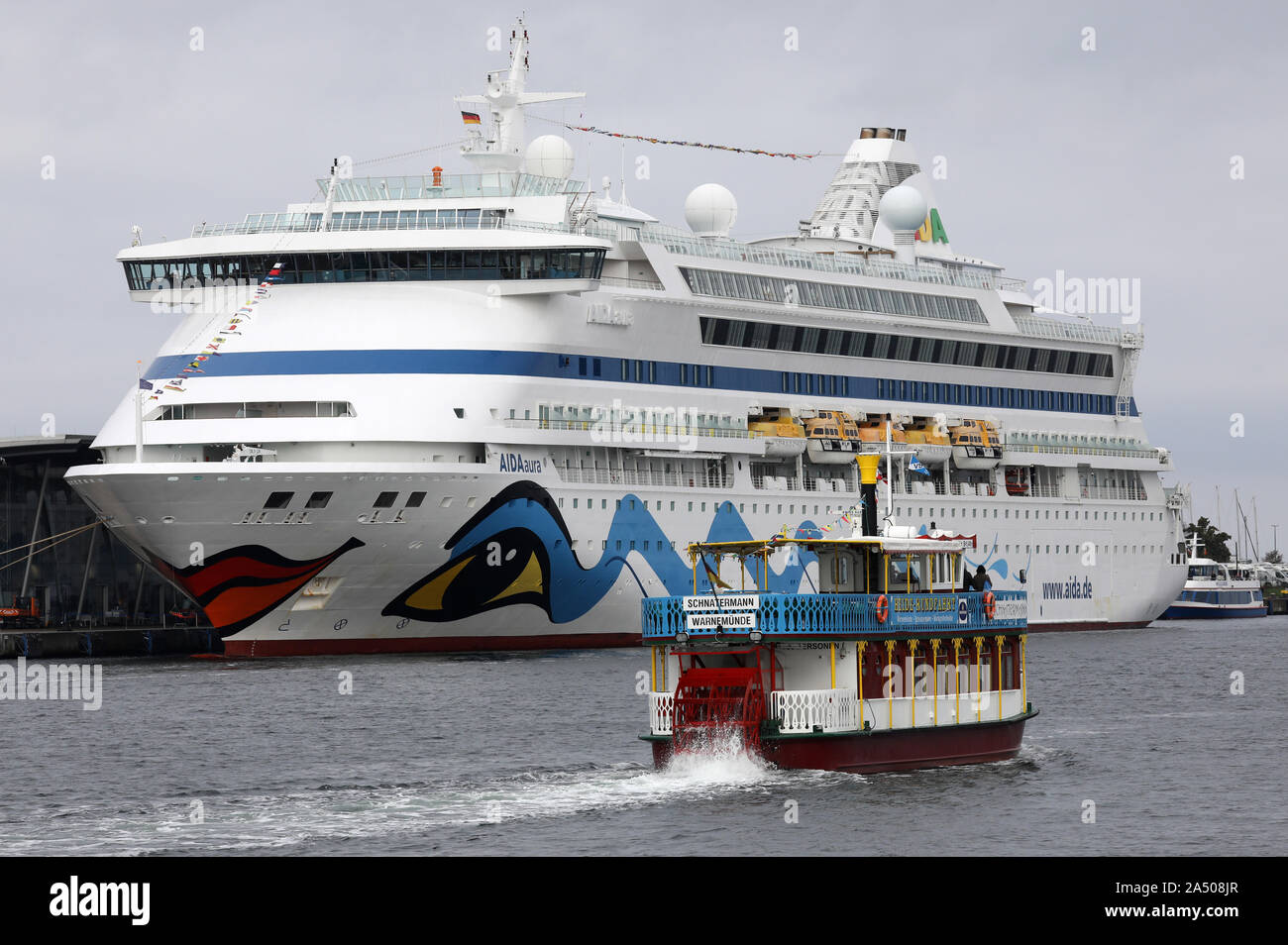 Rostock, Deutschland. 17 Okt, 2019. Die "Aidaaura" ist auf der Beifahrerseite Quay in Warnemünde, einen Ausflug Schiff fährt im Vordergrund. Mit der Ankunft der Luxusliner, die Hochsaison für Cruise Shipping in Rostock geht zu Ende mehr als 900.000 Passagiere an Bord und an Land gegangen von der Ozeanriesen. Das letzte Schiff des Jahres Moor mit der "Balmoral" am 04.12.2019 in Warnemünde. Quelle: Bernd Wüstneck/dpa-Zentralbild/dpa/Alamy leben Nachrichten Stockfoto