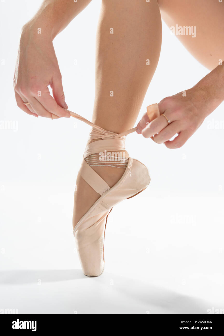 In der Nähe von schönen Beine der jungen Ballerina, die auf Pointe Shoes auf weißem Hintergrund setzt. Ballet Dancer und Praxis Konzept Hintergrund Stockfoto