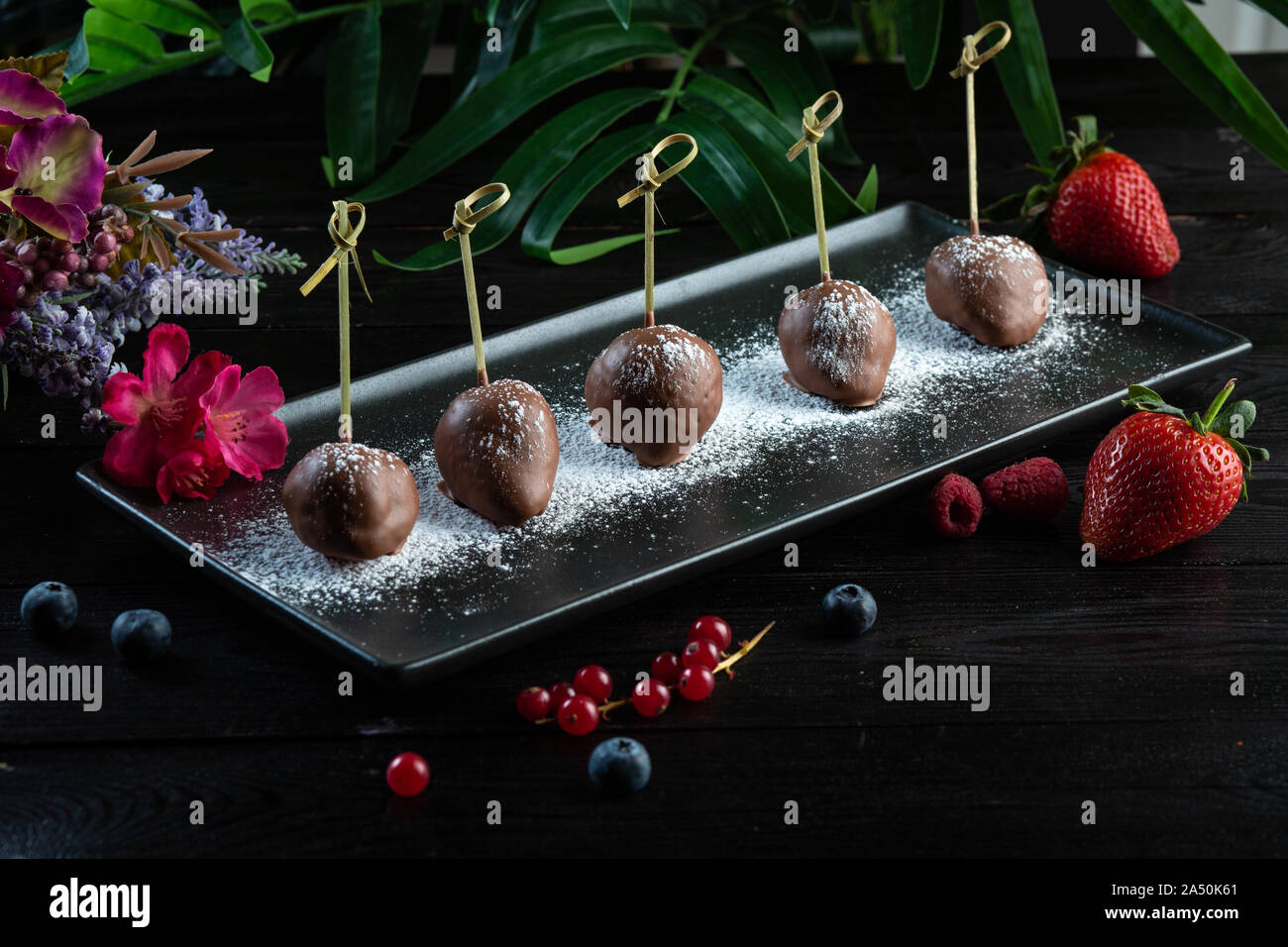 Frische Erdbeeren mit Milch Schokolade auf einem schwarzen rechteckigen Platte auf grauem Hintergrund Stockfoto