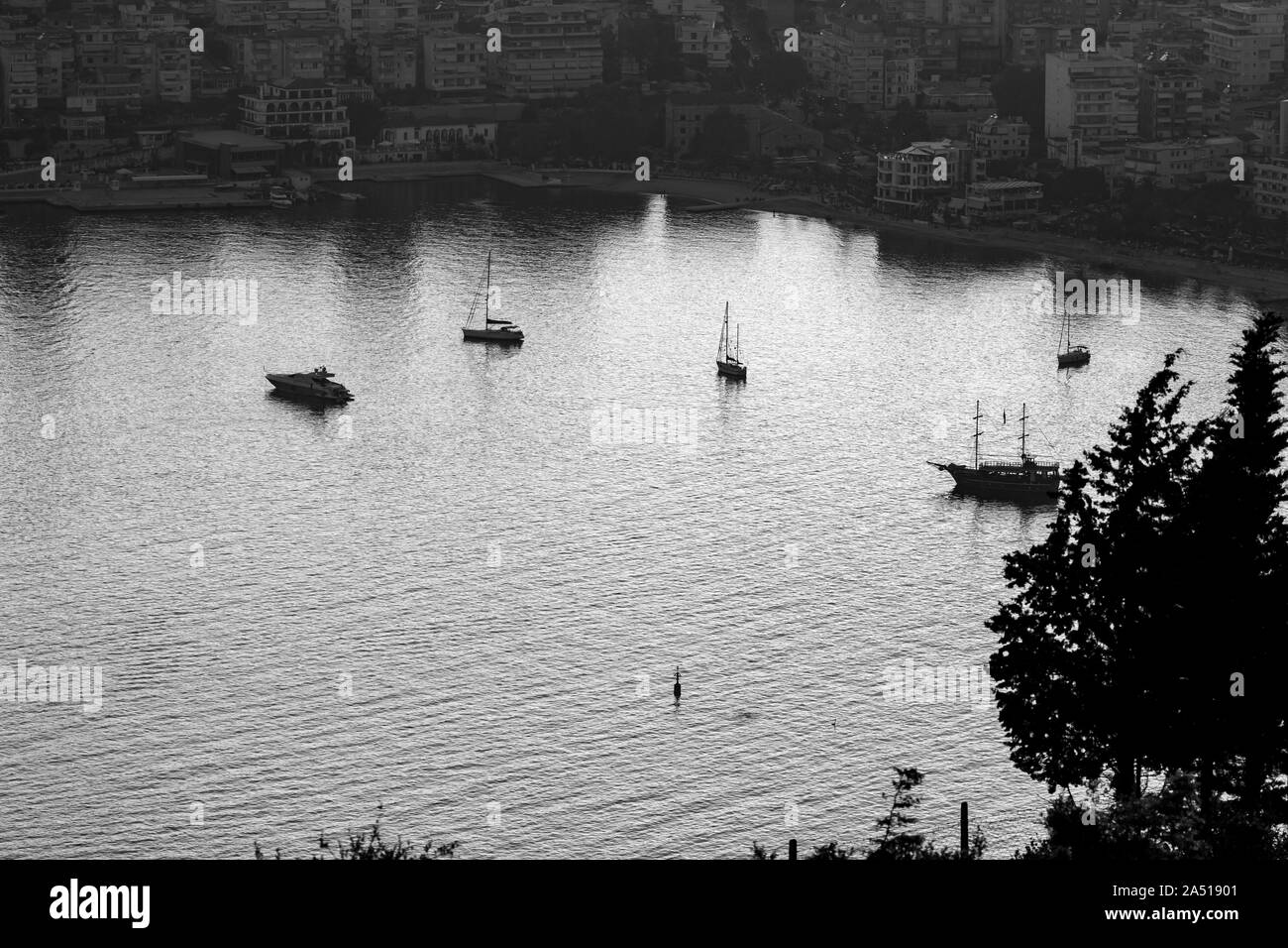 Low Key Luftbild der Bucht von Saranda, Albanien, in die albanische Riviera mit der untergehenden Sonne Lichtreflexionen im Meer Wasser und Silhouetten der Schiffe und Boote in der Bucht Stockfoto