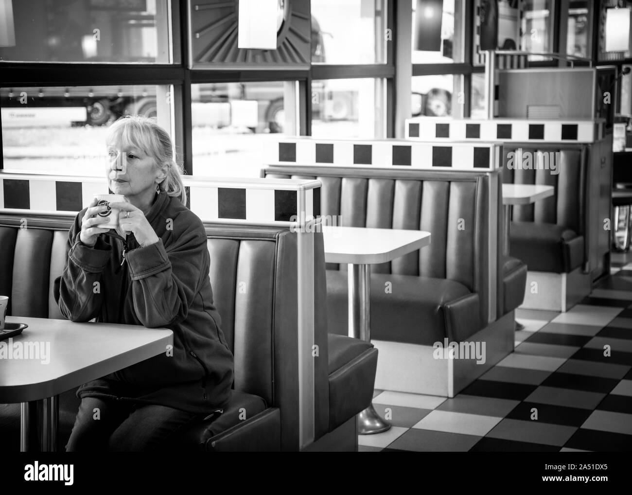 Frau, die allein am Straßenrand sitzt, Tankstelle, die eine Pause von ihrer Reise hat. Stockfoto