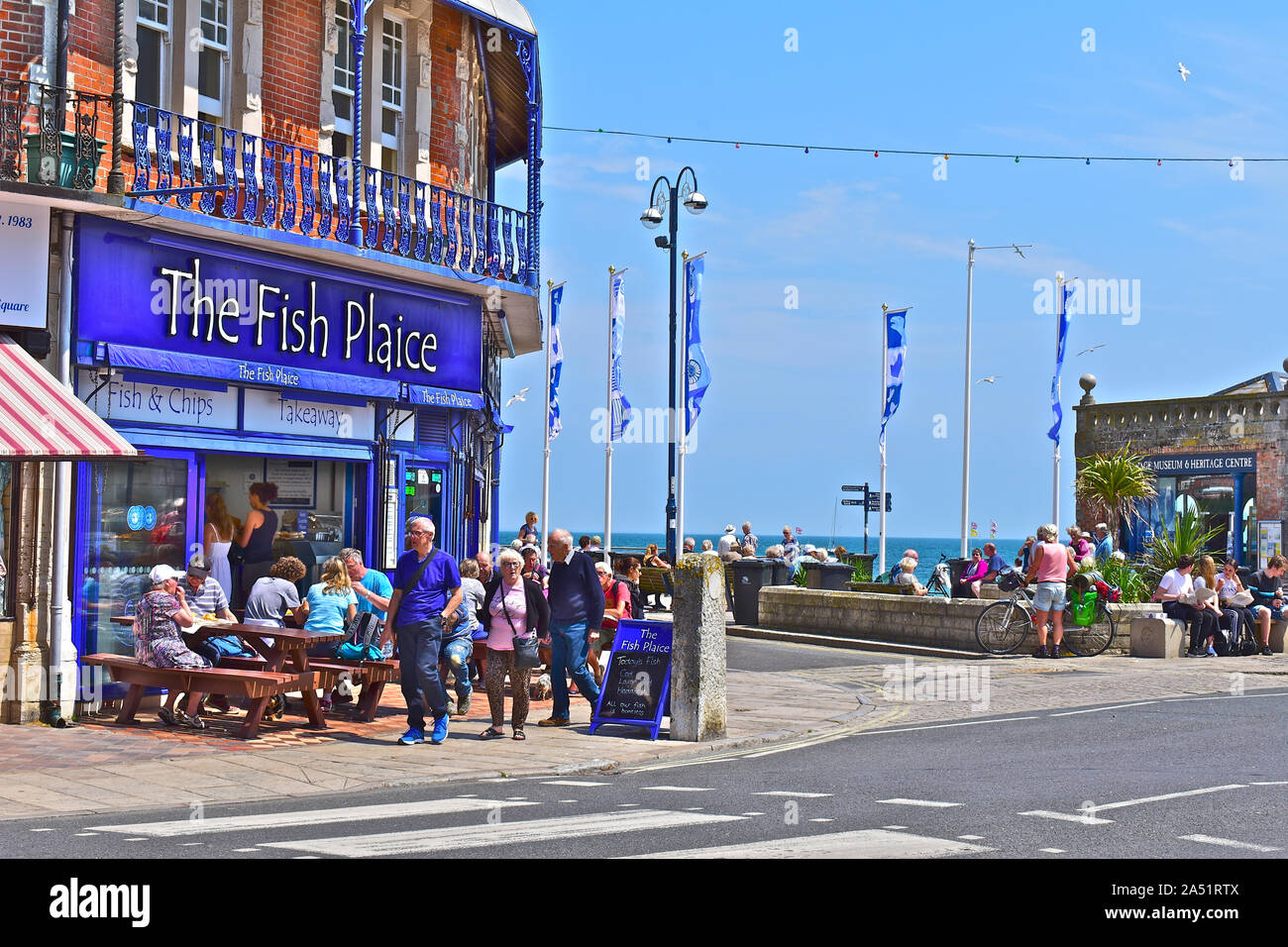 Menschen außerhalb Fish & Chip Shop genießen Sie das Mittagessen im Sommer Sonnenschein. Andere auf dem Platz sitzt, Museum & Heritage Centre. Stockfoto