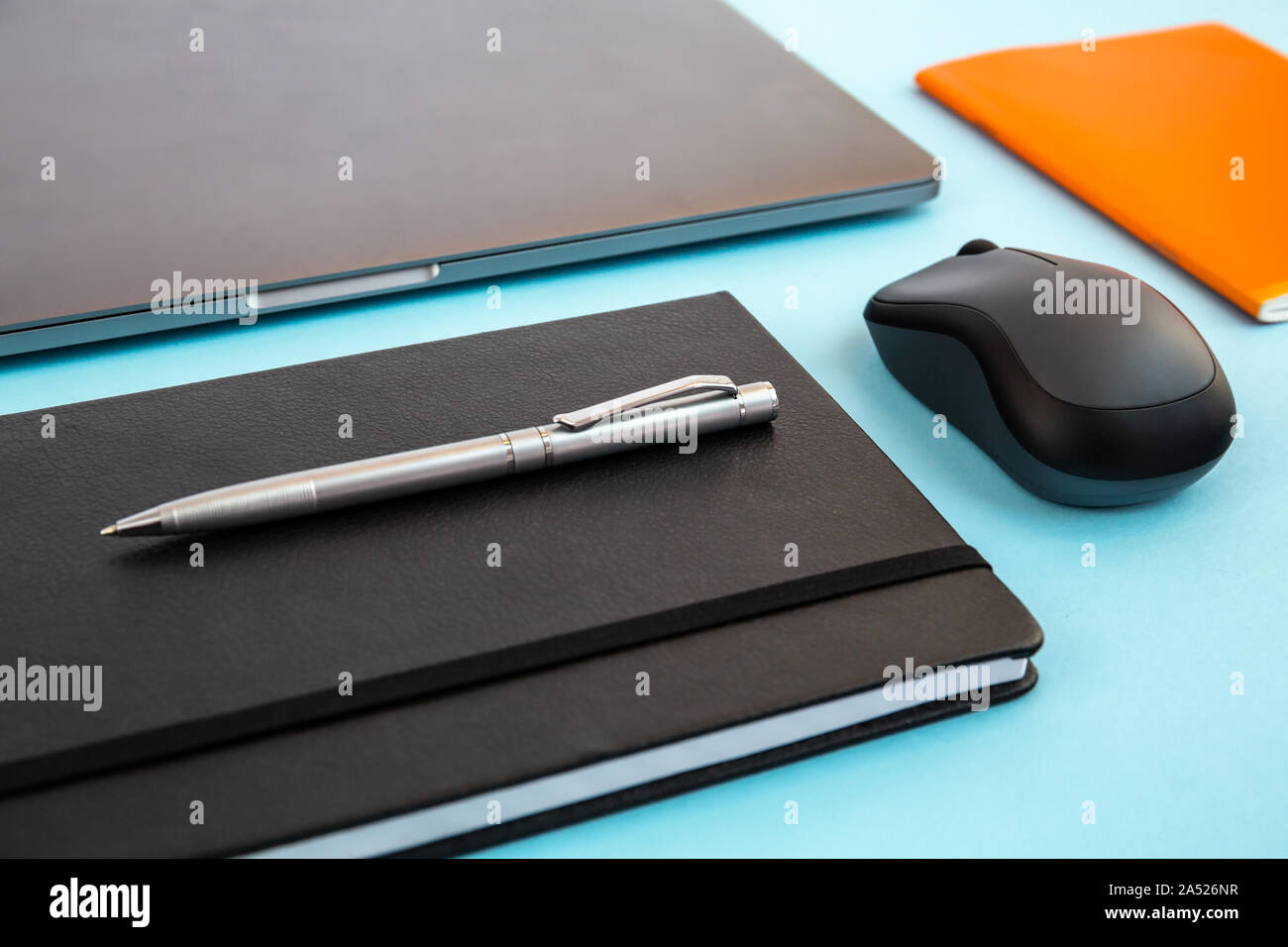 Schreibtisch mit Laptop, Notebook, Agenda, Stift, Bluetooth Maus, orange Notebook. Büro mock up, leeres Dokument. Stockfoto