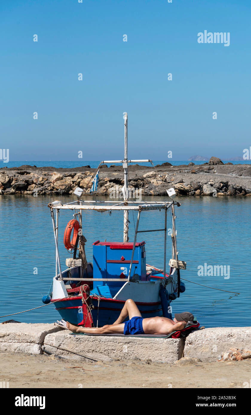 Gouves, Kreta, Griechenland. Oktober 2019. Fischer ein Nickerchen neben seinem Boot am kleinen Hafen Kato Gouves ein ehemaliger US-Militärbasis Stockfoto