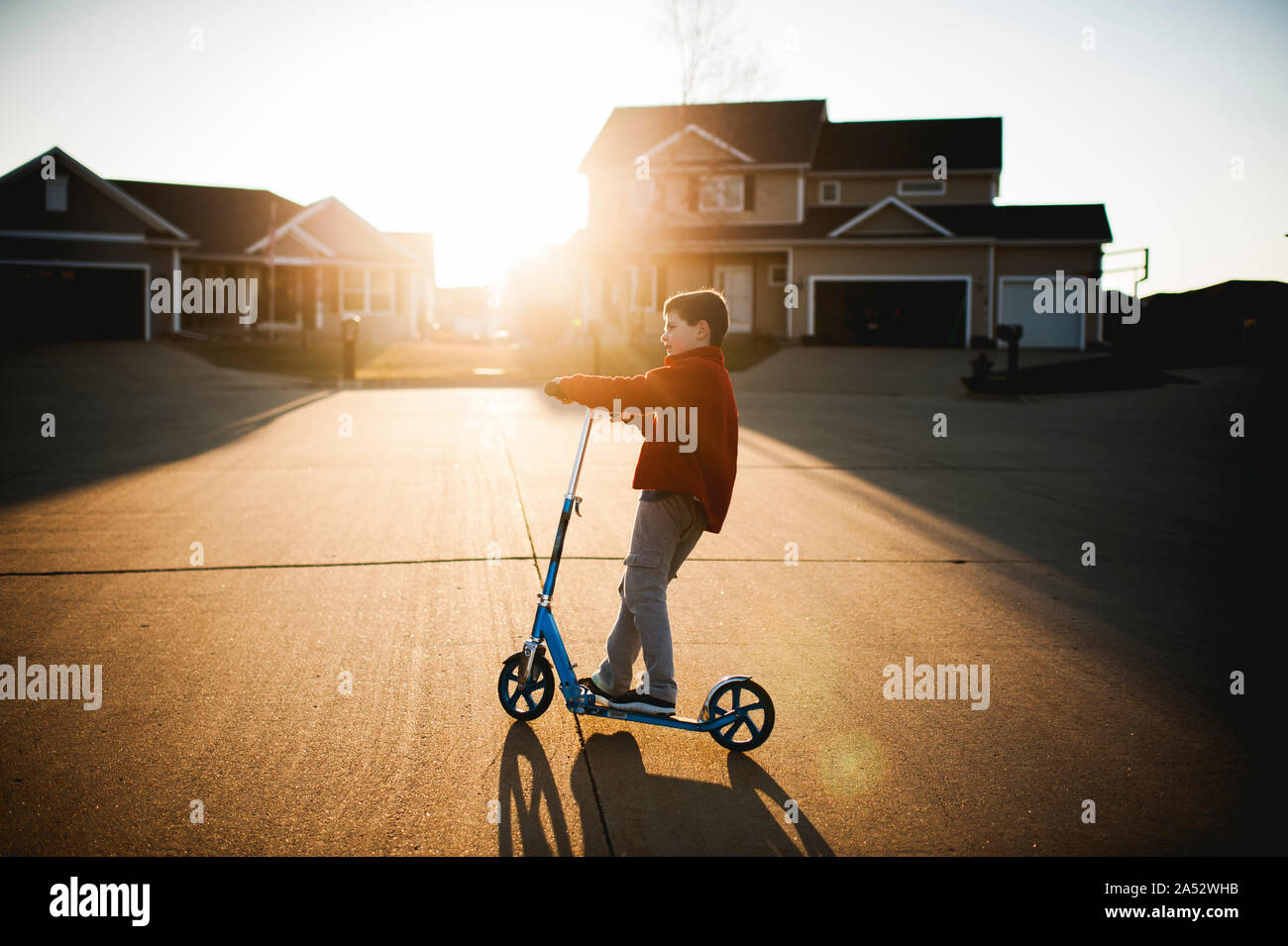 Junge, 7-8 Jahre alt, rollerfahren in der Nachbarschaft in hübsches Licht Stockfoto