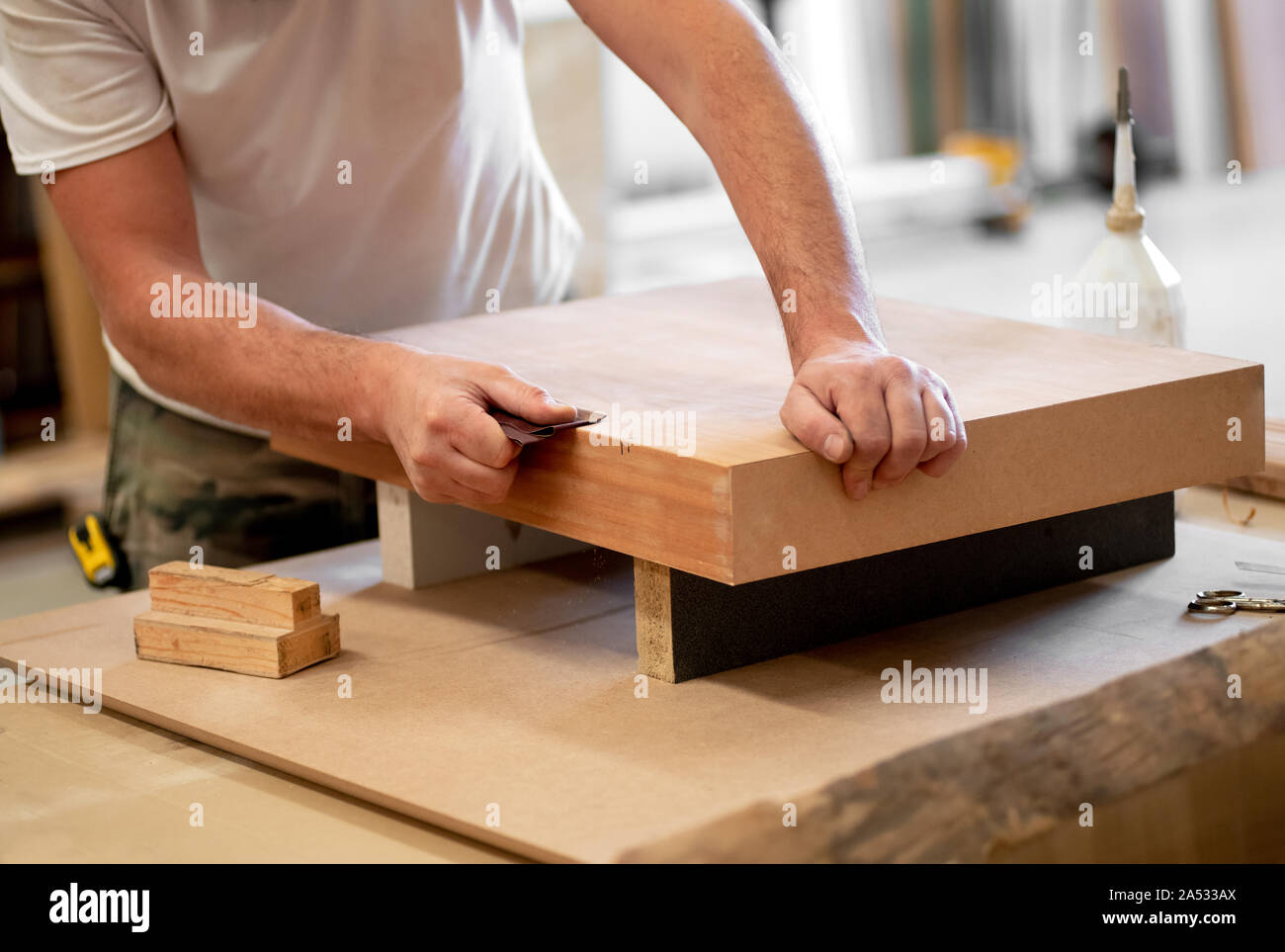 Tischler Schleifen der Kante aus einem Holzblock mit Schleifpapier in einer Holzbearbeitung Workshop in einer Nahaufnahme auf seinen Händen Stockfoto