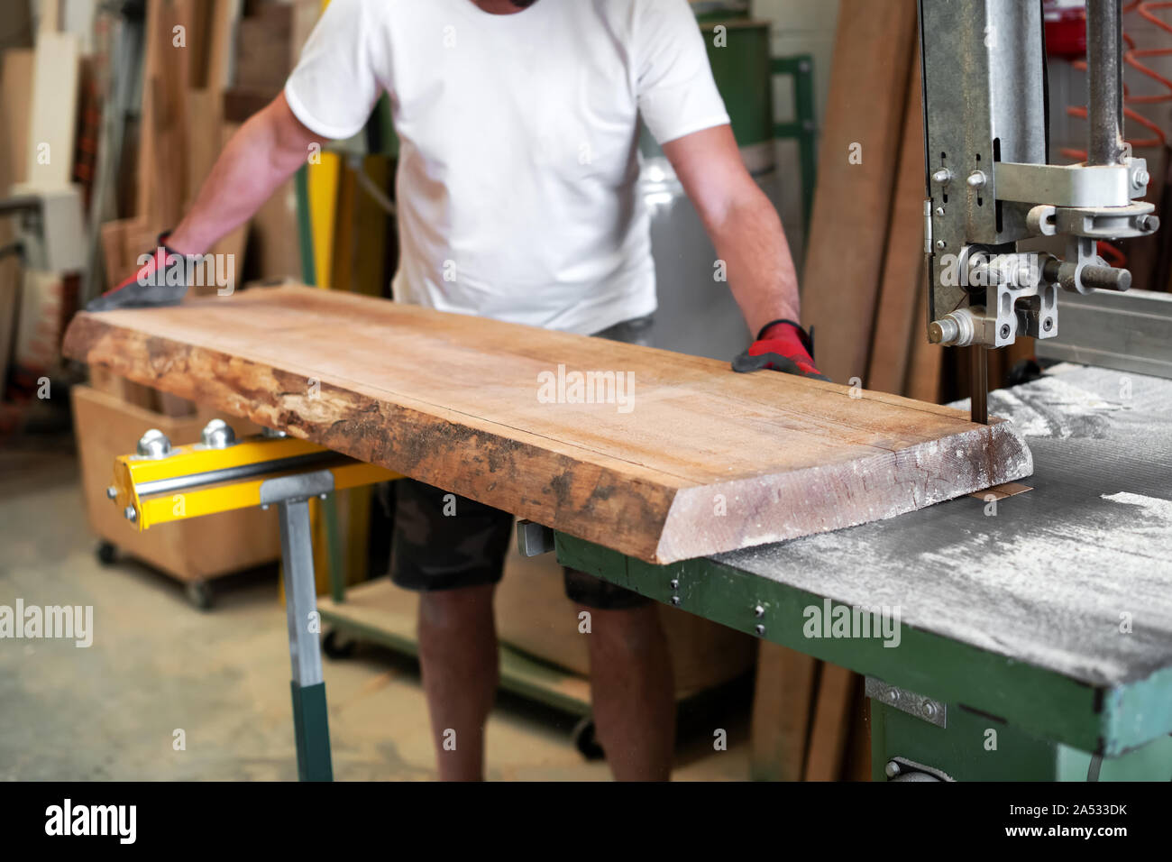 Tischler sägen ein Holzbrett auf einem Band sah es mit seinen Händen mit selektiven Fokus auf die Klinge im Holzbearbeitung Workshop in einer Nahaufnahme auf h Stockfoto