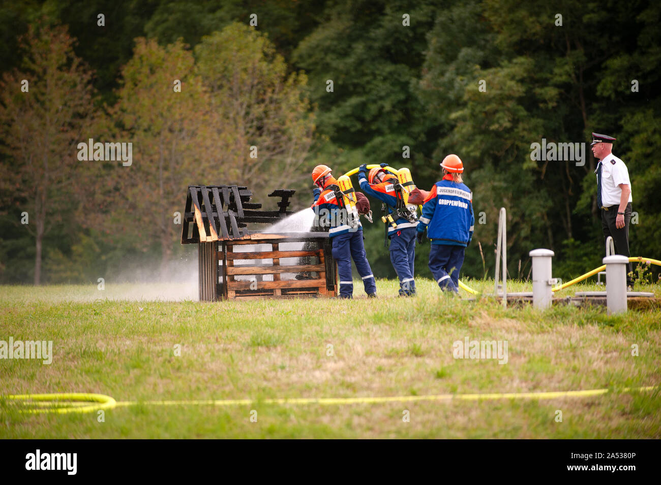 Deutschland, Niederstetten, Baden Württemberg. September 2019 junge feuerwehrleute in Ausbildung mit Feuer Schlauch durch das Feuer zu löschen. Stockfoto