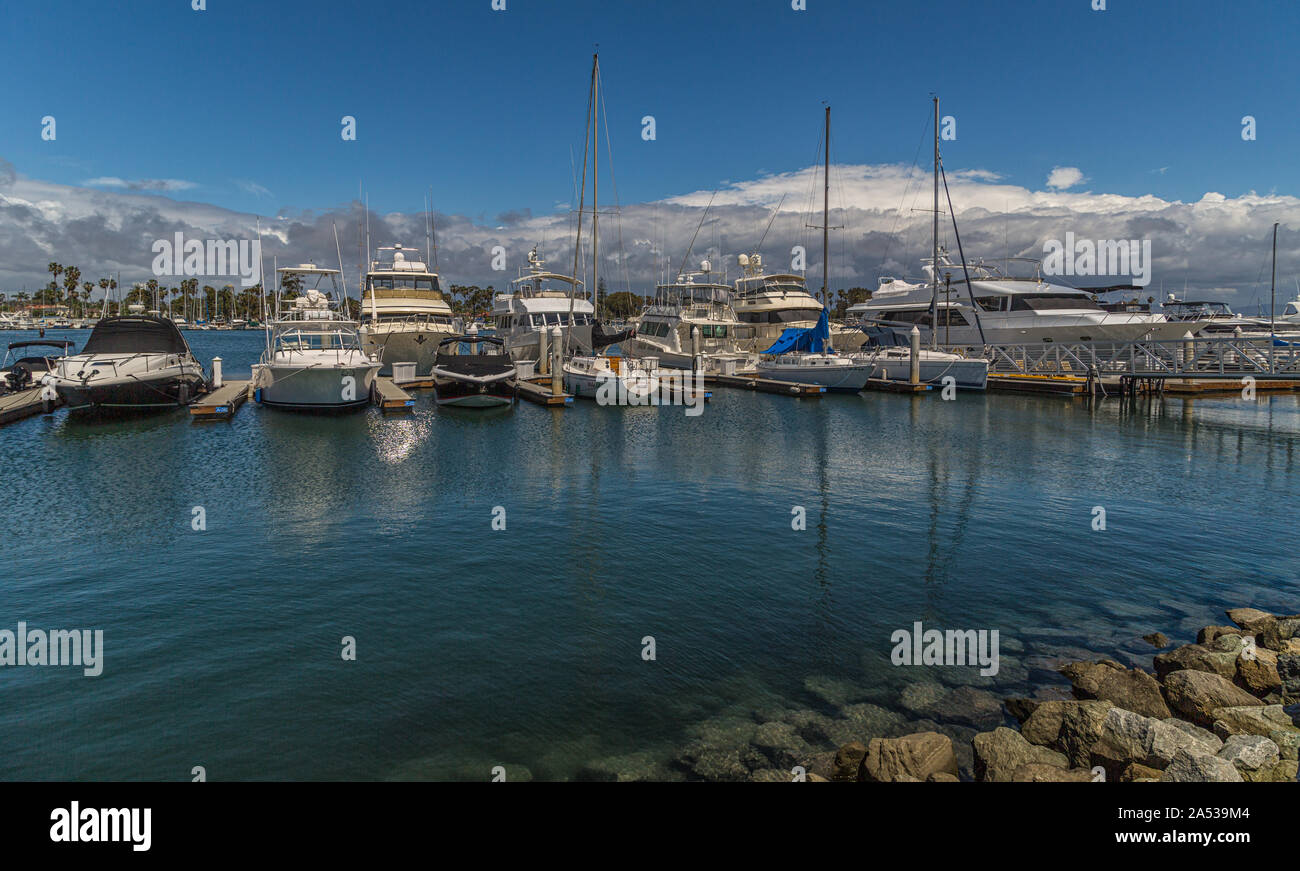 Yachten und Boote aufgereiht an der Marina mit Felsen im Vordergrund und Wolken im Himmel im Hintergrund Stockfoto
