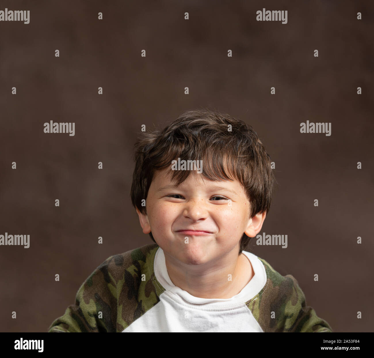 Horizontale studio Shot eines kleinen Jungen machen ein dummes Gesicht um bis scrunching sein Gesicht. Braunen Hintergrund mit kopieren. Schuss aus dem Brustkorb. Stockfoto