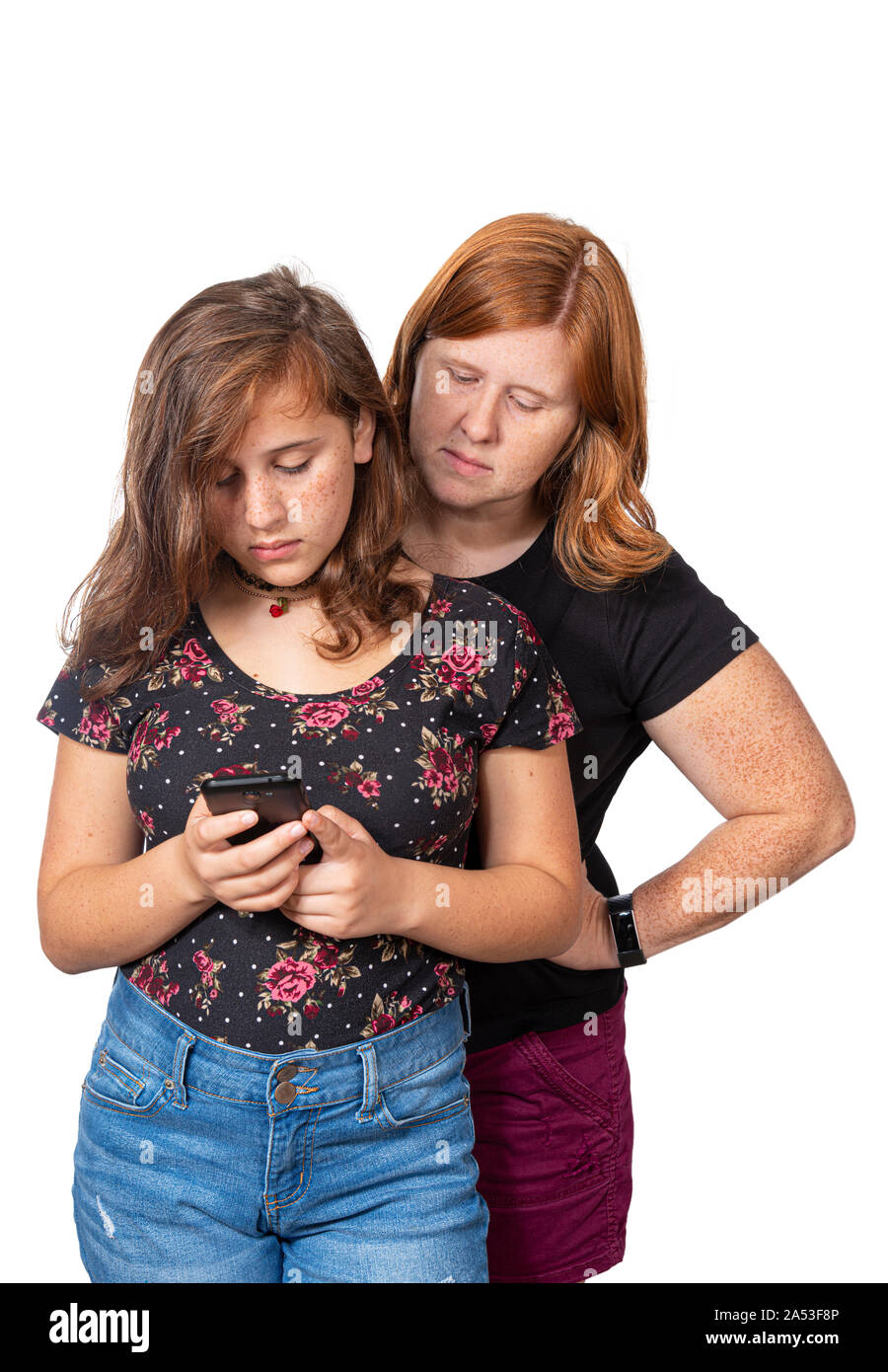 Vertikale studio Schoß einer Mutter, die gerade über die Schulter ihrer Tochter, als sie ihr Mobiltelefon verwendet. Weißer Hintergrund. Stockfoto