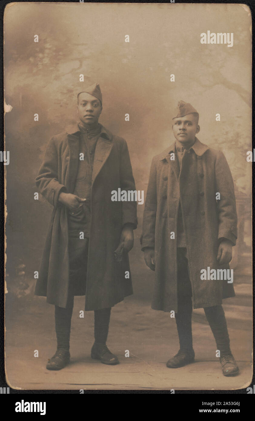 Zwei nicht identifizierte Afrikanische amerikanische Soldaten in Uniformen, greatcoats und Übersee Kappen vor gemalten Hintergrund Stockfoto