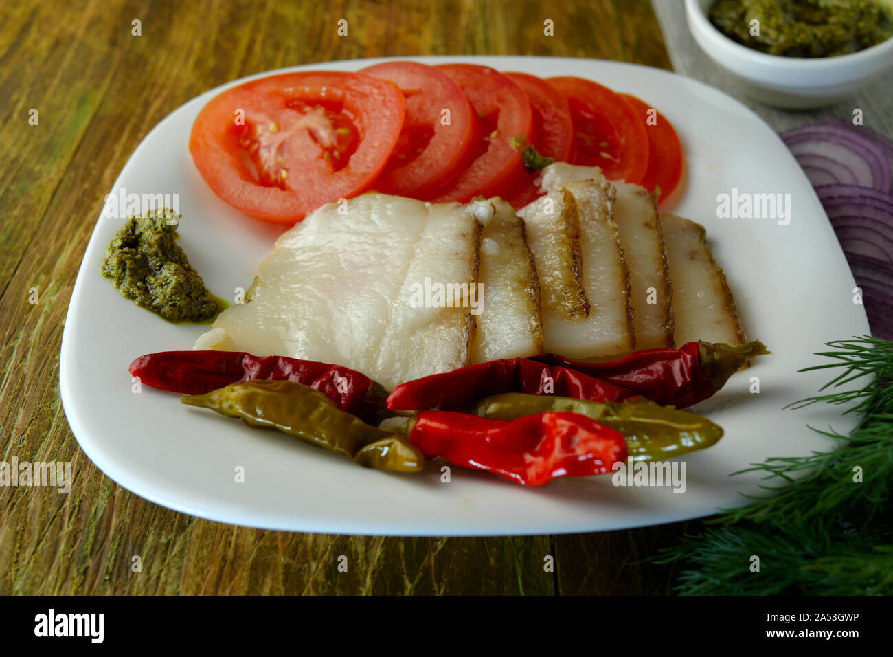 Appetitliche Snacks. In Scheiben geschnitten ​​Smoked Schweineschmalz, Tomaten, eingelegte Paprika und Pesto liegen auf braunem Holz- Oberfläche. Close-up. Stockfoto