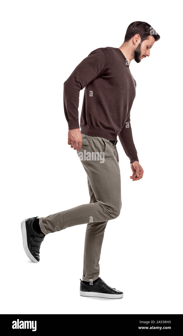 Ein ernster Mann in Freizeitkleidung Spaziergänge in einer Seitenansicht mit einem Bein nach oben gebogen hinter ihm. Stockfoto