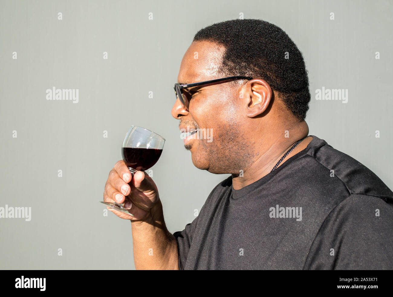 Profil von afrikanischen amerikanischen Mann über zu trinken ein Glas Rotwein gegen einen soliden Hintergrund Stockfoto