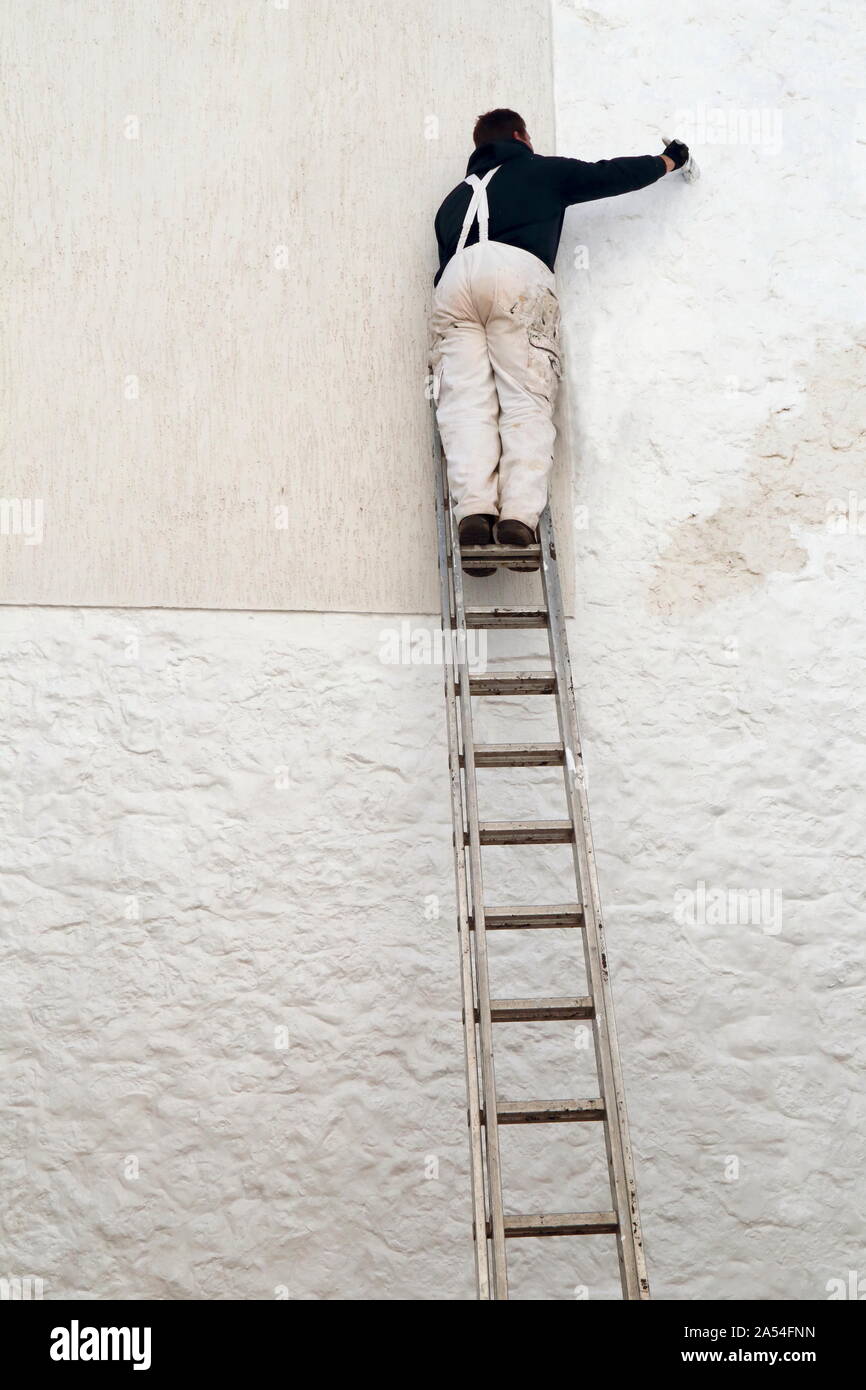 Arbeitnehmer Malerei weißer Fassade beim Stehen auf der Leiter Stockfoto