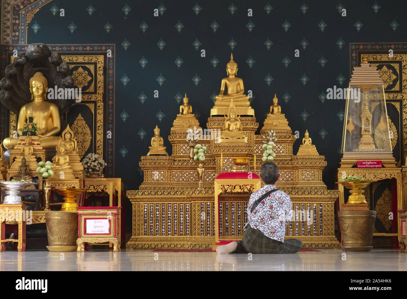 In einem Nebengebäude der Lak Muang (Stadt Säule Schrein) in Bangkok, Thailand, eine Frau betet vor einem reich verzierten goldenen Schrein mit Buddha Statuen Stockfoto