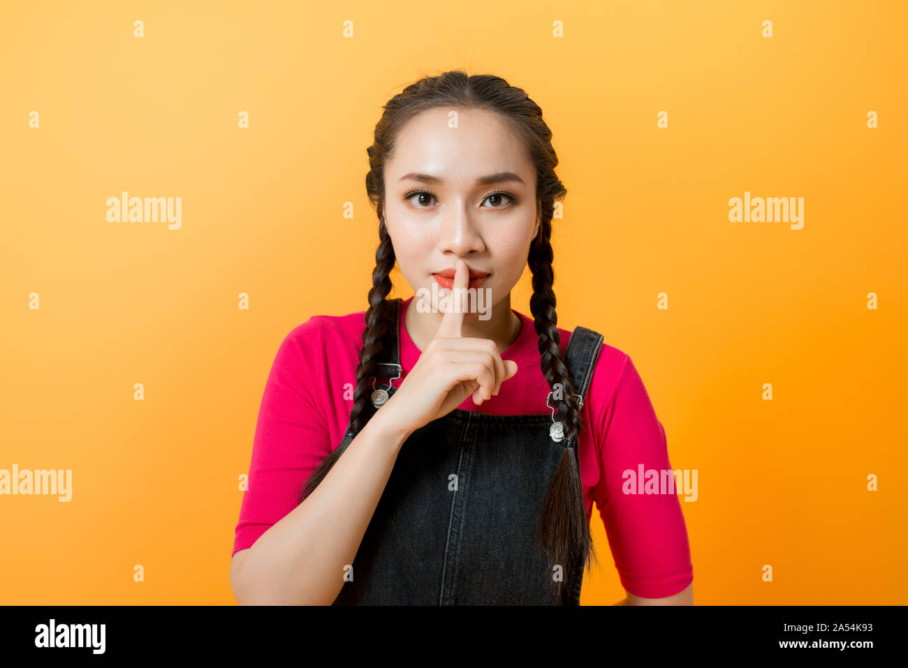 Junge Asiatin auf gelben Hintergrund zeigt ein Zeichen der Stille Geste die Finger im Mund Stockfoto