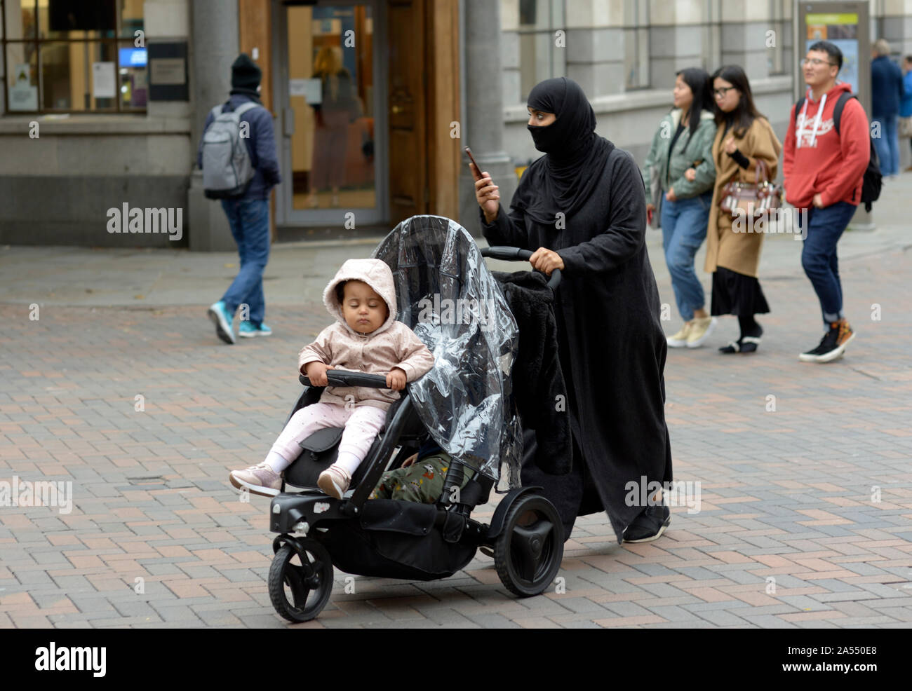 Muslimische Frau mit Niqab, auf mobilen, mit Kind im Buggy. Stockfoto