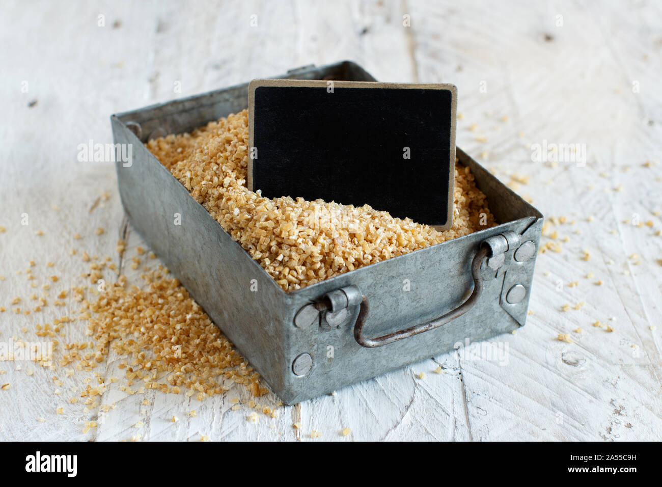 Trockene Bulgur weizen Körner in Metallbox mit einer kleinen Tafel in der Nähe bis Stockfoto