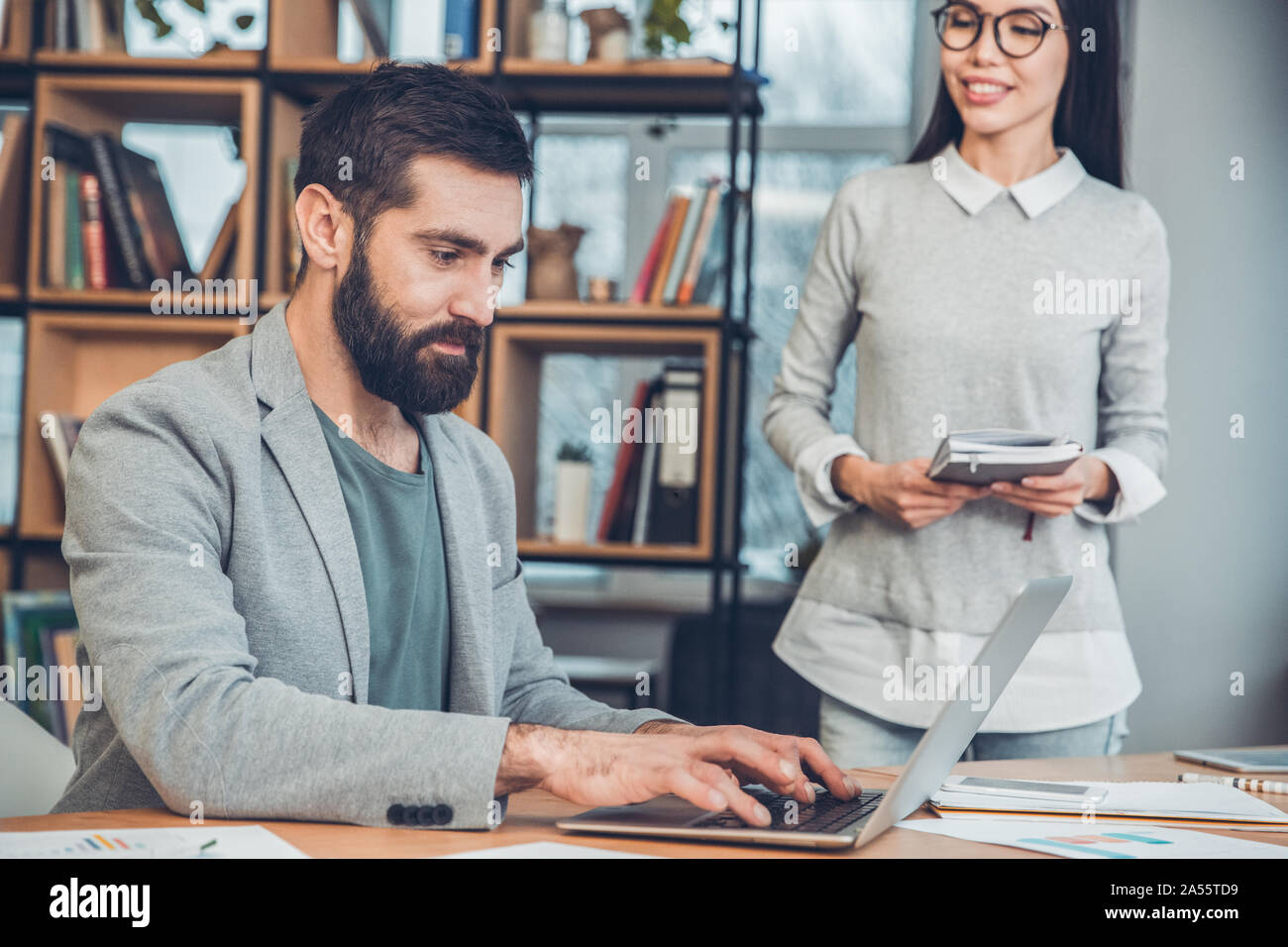 Startupers zusammen arbeiten im Büro Chef Sitzen, Arbeiten am Laptop konzentriert, während die Frau zu Fuß ihn glücklich Stockfoto