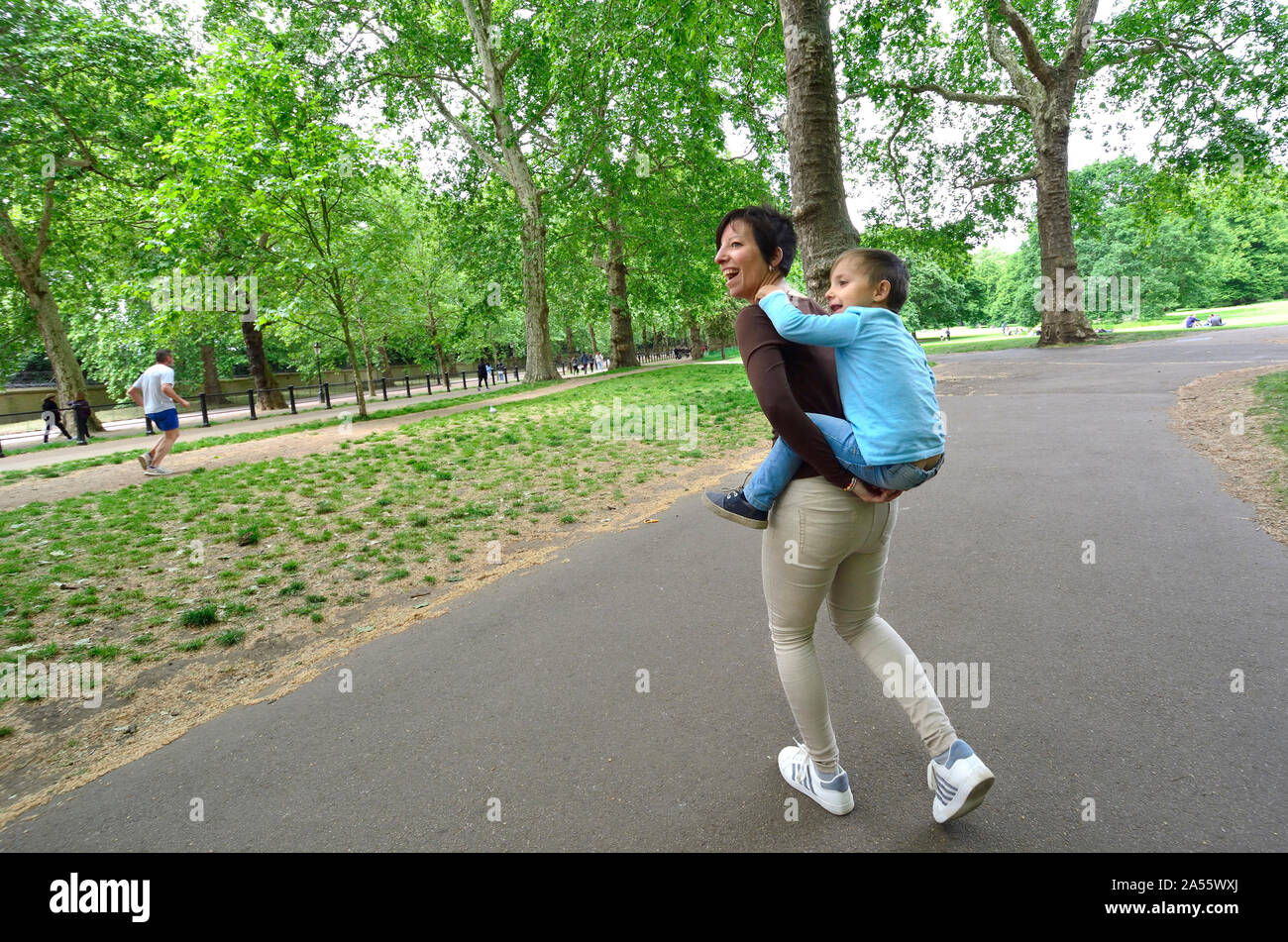 London, England, UK. Mutter ihren Sohn auf dem Rücken im Green Park Stockfoto
