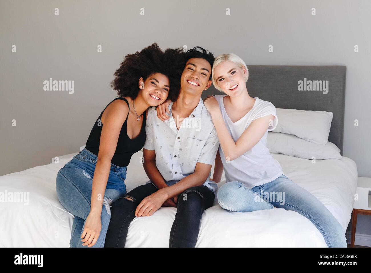 Glückliche junge Mann und zwei Freundinnen sitzen auf dem Bett, Porträt Stockfoto