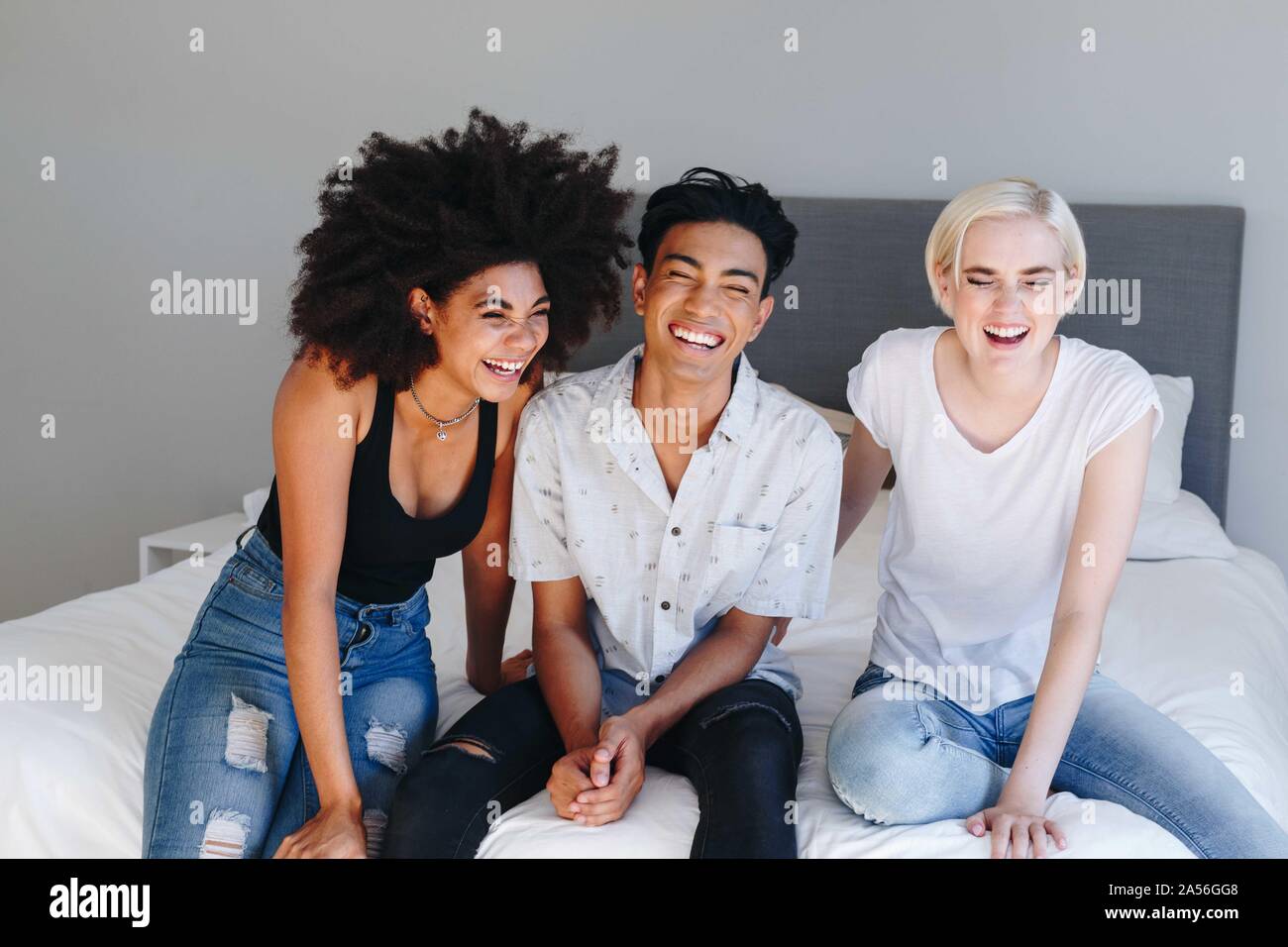 Junger Mann und zwei Freundinnen sitzen auf dem Bett lachen Stockfoto