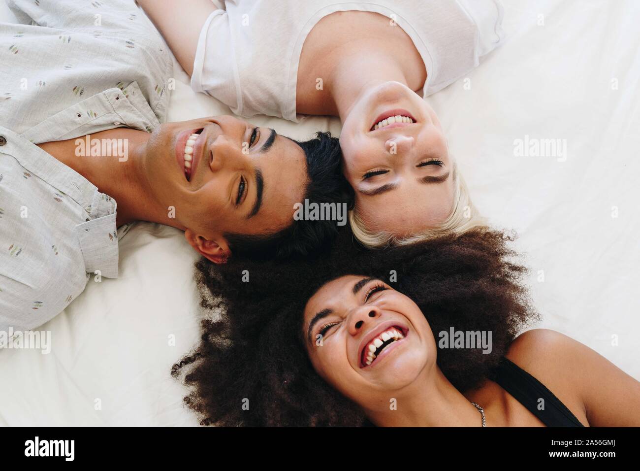 Junger Mann und zwei weibliche Freunde liegend auf Bett lachen, Ansicht von oben Stockfoto