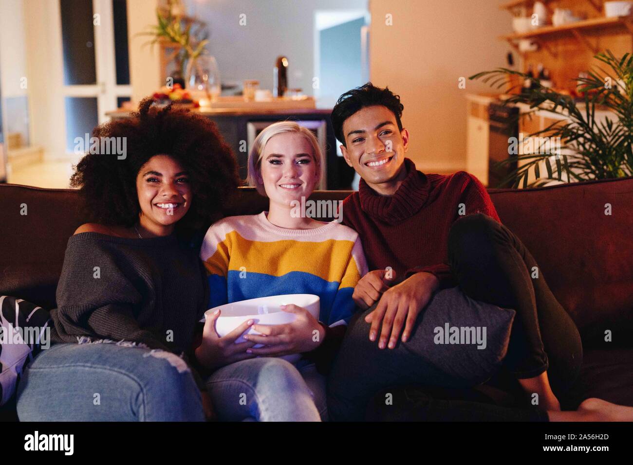 Junge Menschen und junge weibliche Freunde Fernsehen sitzen auf Wohnzimmer Sofa mit Schüssel Popcorn Stockfoto
