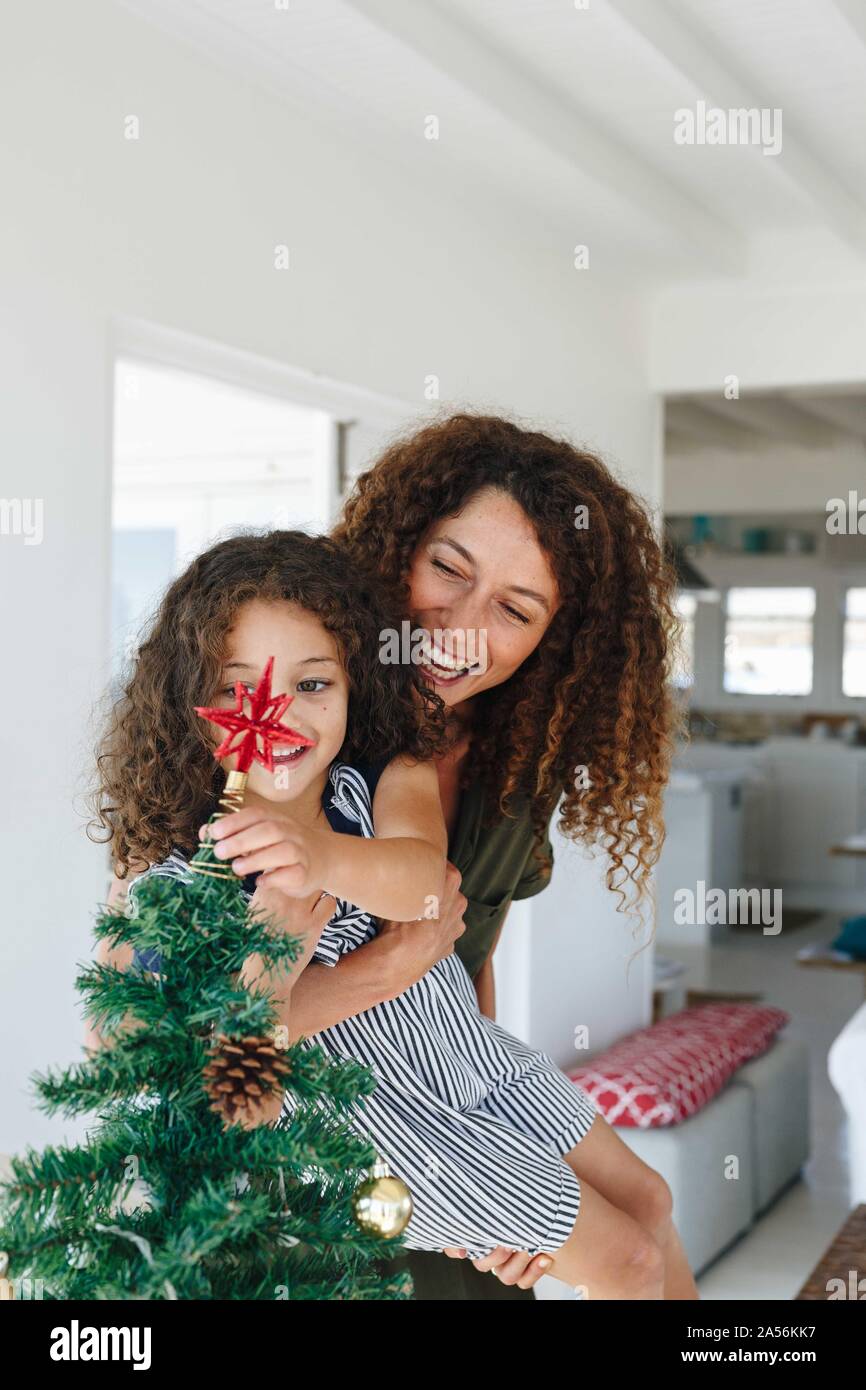 Die Mutter hilft der Tochter statt Stern auf Weihnachtsbaum zu Hause Stockfoto