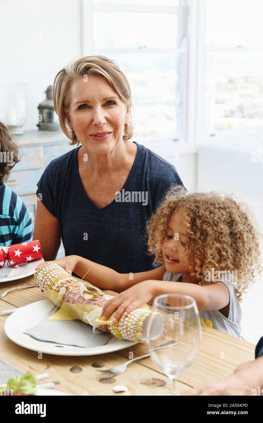 Frau mit Enkeltochter spielen mit Christmas Cracker am Esstisch Stockfoto