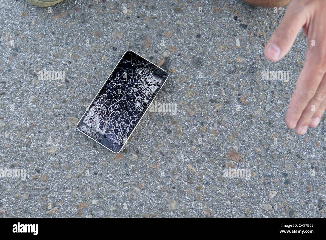 Mann sitzt und halten eine gebrochene smart phone mit einem gesprungenen Bildschirm. Kerl ließ sein Handy auf dem Asphalt und zerbrach es. Ein frustrierter Mann mit Stockfoto