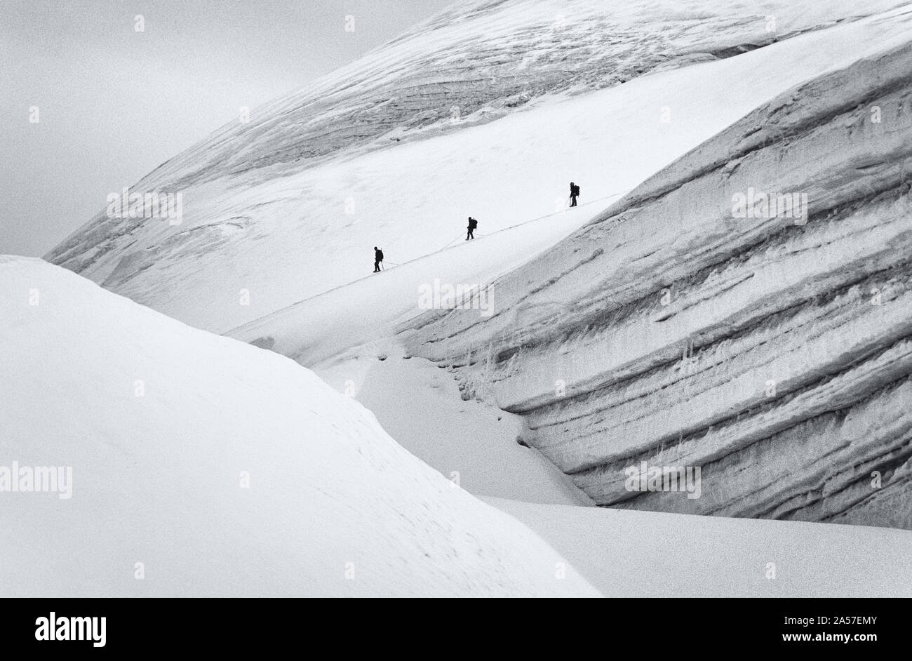 Bergsteigerfiguren passieren eine große Gletscherspalte am Allalinhorn hoch in den Schweizer Alpen Stockfoto