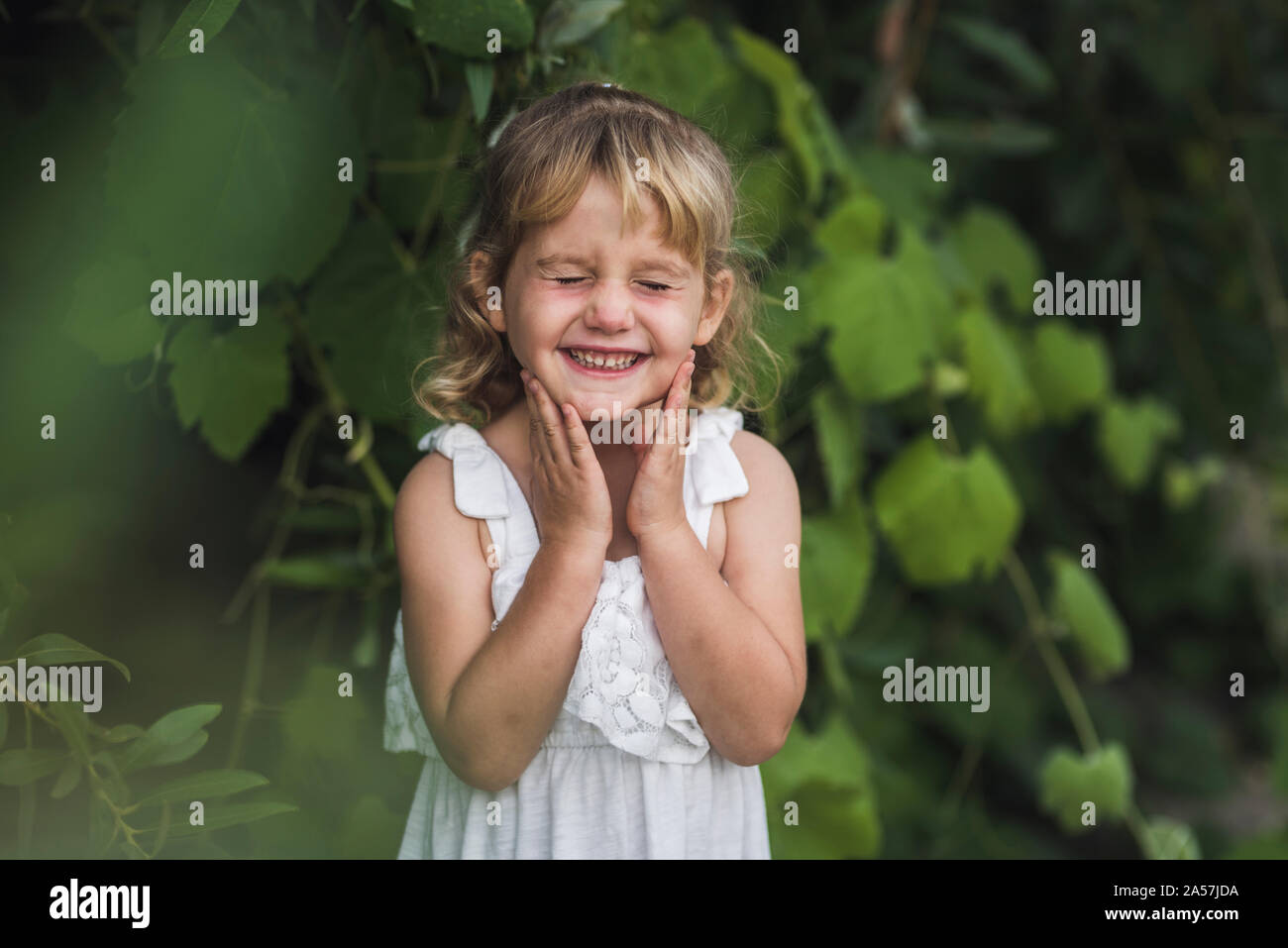 Junges Mädchen mit geschlossenen Augen und Lächeln aufs Gesicht mit den Händen berühren. Stockfoto